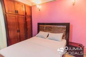 ein Schlafzimmer mit einem Bett und einer rosa Wand in der Unterkunft Appartement meublé à Douala, Bonamoussadi in Douala