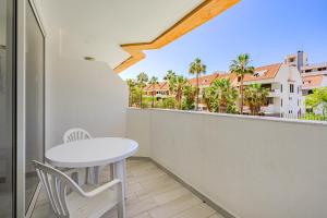 d'une petite table et de chaises blanches sur un balcon avec des palmiers. dans l'établissement Un dormitorio en Playa de las Américas, à Adeje