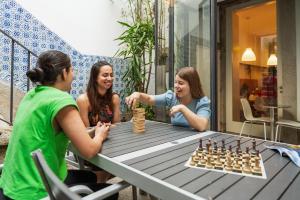 Três raparigas a jogar xadrez numa mesa. em Porto Lounge Hostel & Guesthouse by Host Wise no Porto