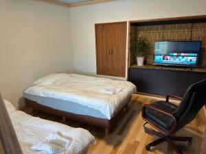 - une chambre avec un lit, une chaise et une télévision dans l'établissement ゲストハウスみどり, à Iiyama