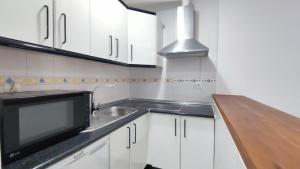 cocina con armarios blancos, fregadero y microondas en Fantástico apartamento totalmente renovado, en Torre del Mar