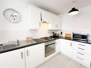 a kitchen with white cabinets and a clock on the wall at Aristotle House by Blue Skies Stays in Stockton-on-Tees