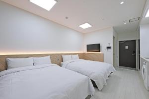 two beds in a hotel room with white sheets at World Sky Residence Hotel in Sokcho