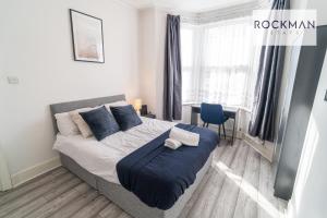 a bedroom with a bed with blue pillows and a desk at 32 The Grove - Modern & Elegant Home Close to Beach with Parking by RockmanStays in Southend-on-Sea