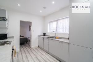 a white kitchen with a sink and a counter at 32 The Grove - Modern & Elegant Home Close to Beach with Parking by RockmanStays in Southend-on-Sea