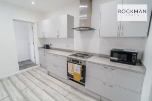 a white kitchen with a stove and a microwave at 32 The Grove - Modern & Elegant Home Close to Beach with Parking by RockmanStays in Southend-on-Sea
