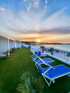 a row of blue lounge chairs on a balcony with the sunset at Hotel Egitarso Sul Mare in San Vito lo Capo