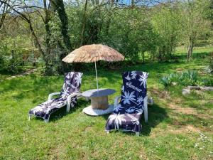 twee stoelen en een tafel met een paraplu in het gras bij Tonneau Vacances Insolites in Véria