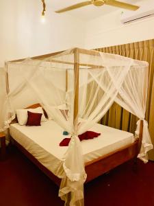 1 dormitorio con cama con dosel y mosquitera blanca en Tropicana Home Stay en Arugam Bay