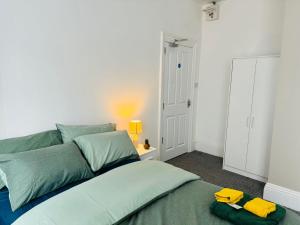 ein Schlafzimmer mit einem Bett mit grüner Bettwäsche und gelben Handtüchern in der Unterkunft Manzil by HeyHouseLife in Middlesbrough