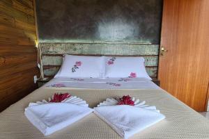 a bed with white towels and red flowers on it at Moradas do Maneca in Imbituba