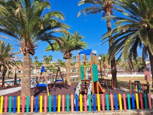 un parque infantil con una valla colorida y palmeras en Precioso bungalow en Maspalomas en San Bartolomé