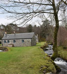a stone house next to a river with a tree at The Smiddy in Lochailort
