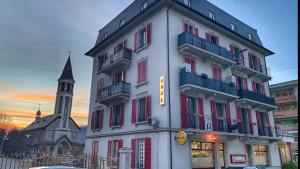 a tall white building with red windows and a church at Today Appartement in Chippis