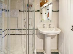 La salle de bains blanche est pourvue d'un lavabo et d'une douche. dans l'établissement The Nook, à Llanrwst