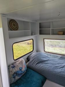 a bed and two windows in the back of an rv at Caravan Zee by BnB de Kapitein in 't Horntje