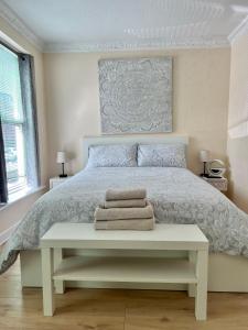 a white bedroom with a bed with a bench with towels at Coco’s Homestay - Sidmouth in Reading