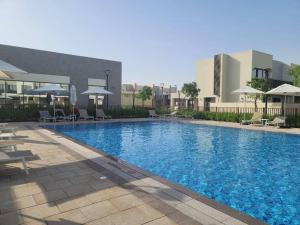 a large swimming pool with chairs and umbrellas next to a building at Green Haven 3BR Villa-Golfside Grandeur-Emmar South in Dubai