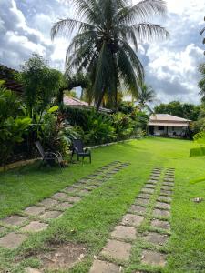a garden with a palm tree and a stone path at Cassinha Aconchegante para 2, Varanda com redes, 9 min Praia in Guarajuba