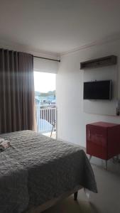 1 dormitorio con cama, TV y balcón en Pousada Família Eleutério en Penha