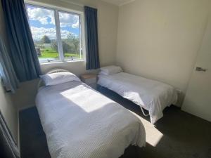 two beds in a room with a window at Rata Karaka Bach in Ngunguru