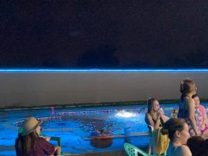 un grupo de personas sentadas alrededor de una piscina por la noche en Al Rahba Holiday Farmhouse en Al Rahba