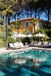 a pool with chairs and umbrellas in front of a house at La Bastide de Saint Tropez in Saint-Tropez