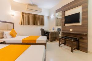 a room with two beds and a desk and a television at Hotel Prime in Ahmedabad