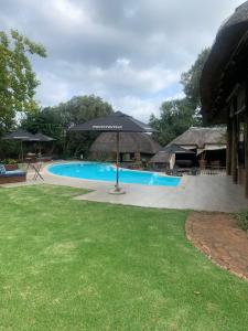 uma piscina com um guarda-sol num quintal em Tidimalo Lodge em Rustenburg
