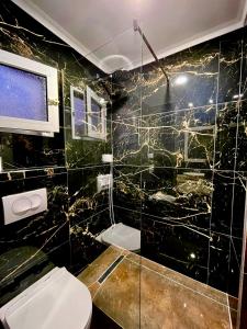 Baño de azulejos negros con aseo y ventana en Hotel Kolagji, en Himare