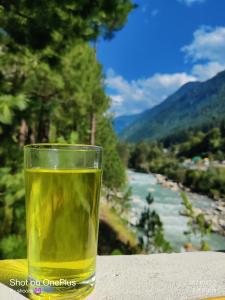 a glass of wine sitting on a table with a view of a river at Shoolin Cottages & Camp's in Kasol