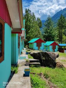 a row of colorful buildings with trees and mountains at Shoolin Cottages & Camp's in Kasol