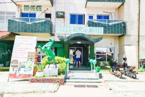 um homem parado em frente a um hotel verde em New Green Horse Hotel em Cotonou