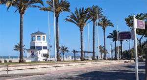 eine Straße mit Palmen und einem Leuchtturm am Strand in der Unterkunft Apartamento Los Juncos - 50m playa - Sólo familias - Parking gratuito - WIFI - TV 55" 4K - PS5 in Playa de Gandia + 18 Fotos