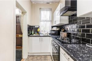 a kitchen with white cabinets and black tiles on the wall at Bright sunny, double bed with garden, TV and Wi-Fi in Leeds