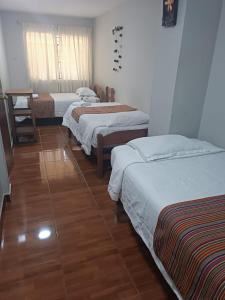 a room with three beds and a wooden floor at Hospedaje Quillabamba in Santa Teresa