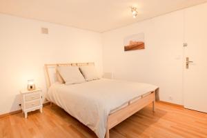a white bedroom with a bed and a wooden floor at Le stade in Issoire