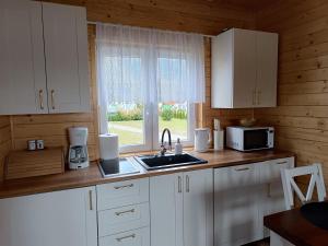 cocina con armarios blancos, fregadero y ventana en Szary domek nad jeziorem, en Kołczewo
