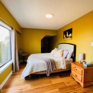 1 dormitorio con paredes amarillas, 1 cama y ventana en Oceanside Manor (Beach View) en Qualicum Beach