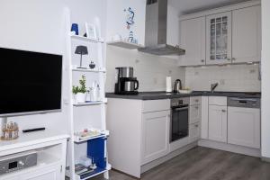 uma cozinha com armários brancos e uma televisão de ecrã plano em FeWo am Dorfteich em Lemkenhafen auf Fehmarn