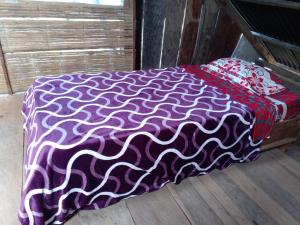 montecristo hostel في سانتا مارتا: سرير مع بطانية أرجوانية وبيضاء على أرضية خشبية