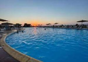 a large blue swimming pool with a sunset in the background at Blumar Sidi Abdel Rahman 2 bedrooms Chalet North Coast in El Alamein
