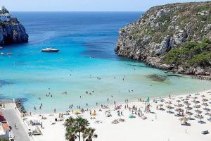 un groupe de personnes sur une plage dans l'eau dans l'établissement Ático con vistas al mar Cala enPorter, à Cala'n Porter