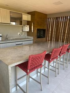 a kitchen with a counter with four red chairs at Apartamento Itacimirim Exclusive - Pé na areia in Camacari