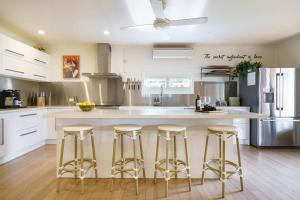 a kitchen with a large white counter with bar stools at Karinya - Luxurious soul sanctuary by the surf. in Rye