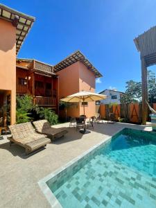 a patio with a swimming pool and a house with an umbrella at Pousada Vila dos Corais - Taipu de Fora in Marau