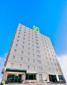 un edificio blanco alto con un letrero verde. en Kurashiki Ekimae Universal Hotel, en Kurashiki