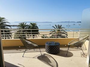 2 sillas y una mesa en un balcón con vistas a la playa en Appartement T3 lumineux traversant totalement neuf en face de la plage Front de mer vue sur les iles Vue mer panoramique assurée Résidence de la plage centre ville du Lavandou 3eme étage avec ascenseur Appartement T3, en Le Lavandou