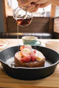 a person pouring syrup on a piece of toast with fruit at R Hotel Namba South in Osaka