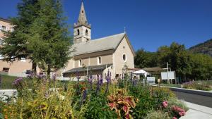 une église avec une tour d'horloge et un bouquet de fleurs dans l'établissement Noyers du Soleil, Chambre d'hôte avec petit déjeuner à proximité de Gap, à La Bâtie-Vieille